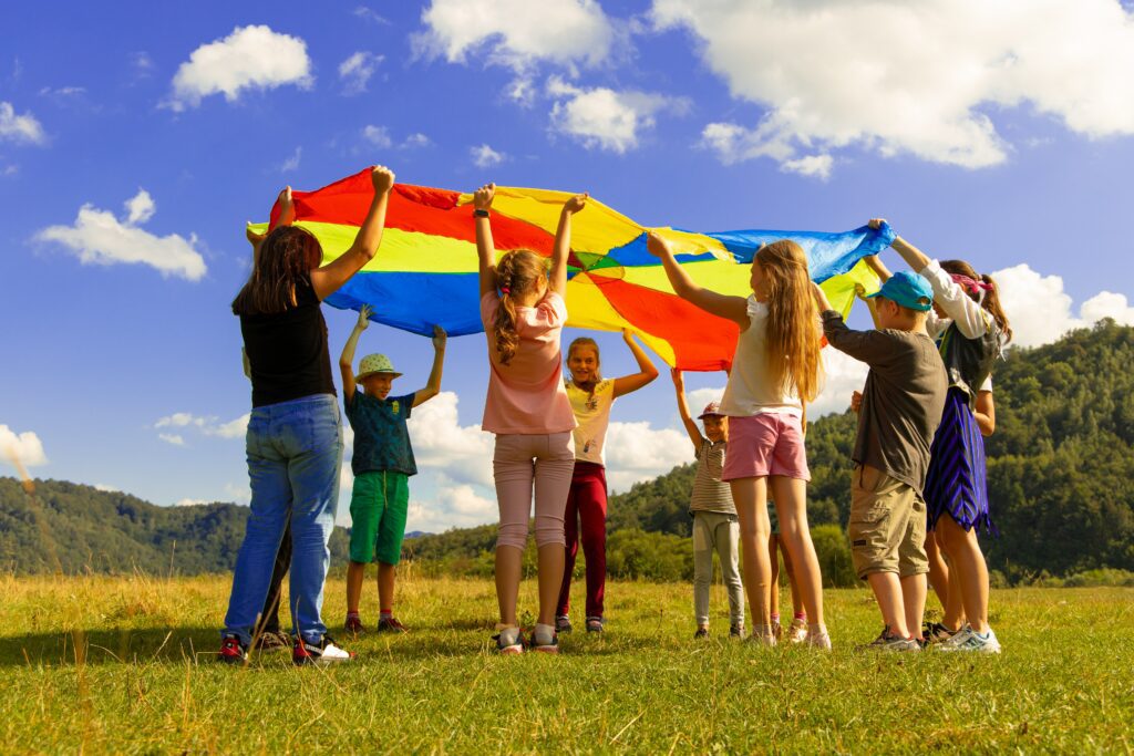 Kids and adults standing in a circle lifting a parachute over their heads