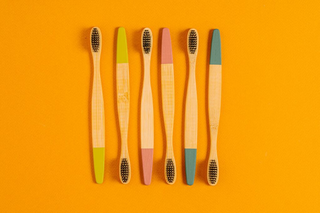 6 wooden toothbrushes in a row on an orange background.