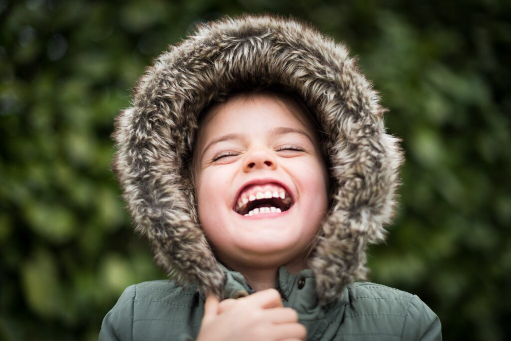 A child in a warm fuzzy hood, laughing with her eyes closed.
