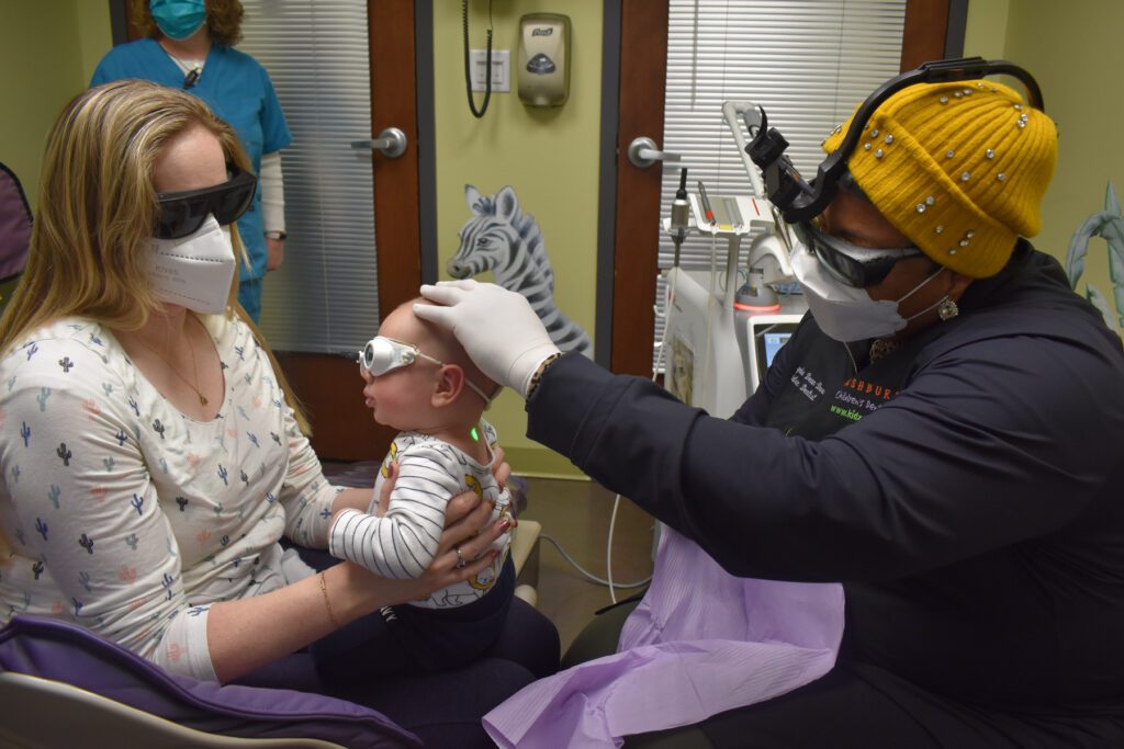 Mother holding a child while the dentist checks the child