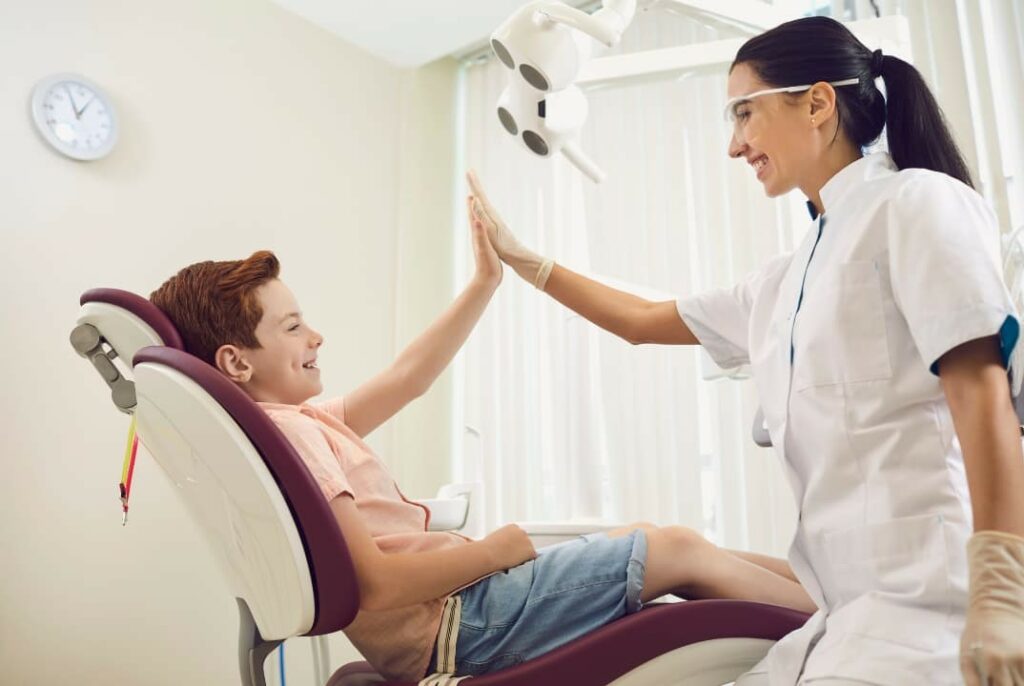 A brave and happy kid sitting on a dental chair giving his dentist a high five