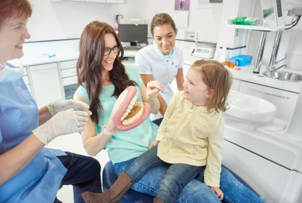 A little girl and her mom sitting on a dentist chair while talking to the dentist