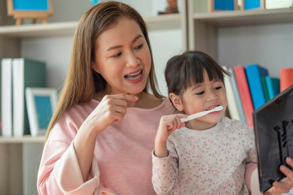 A mother teaching her daughter how to brush her teeth to prevent tooth decay
