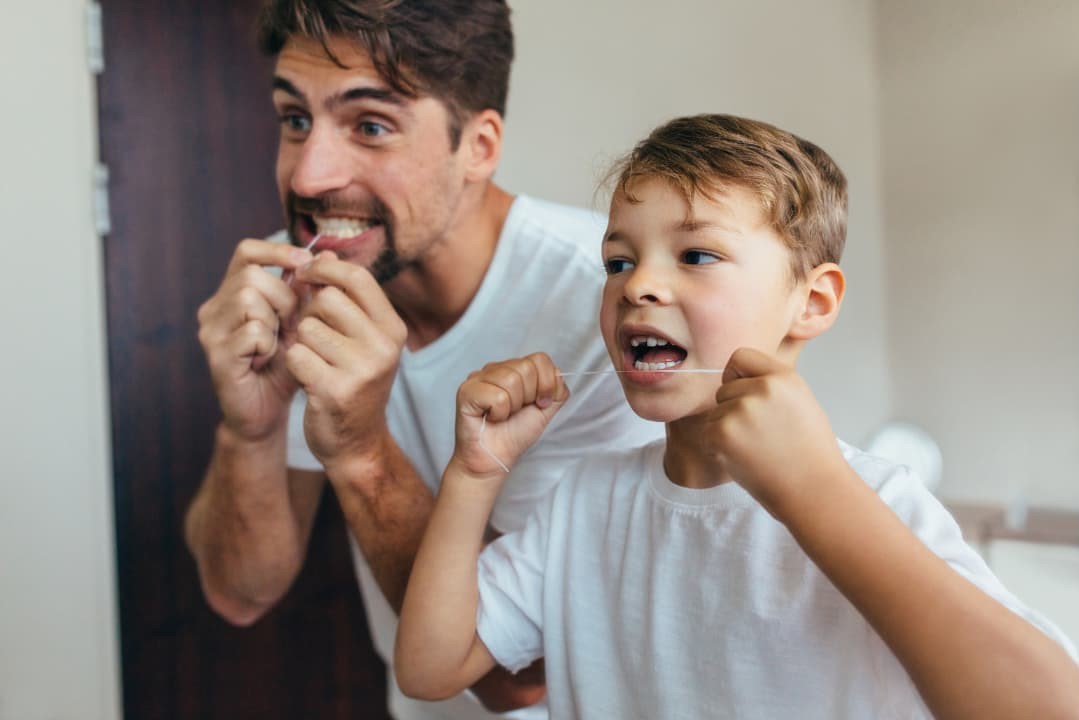 A father and son flossing their teeth together after brushing