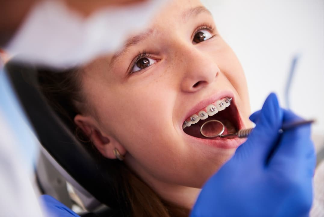 A kid having her teeth with braces get checked by a dentist